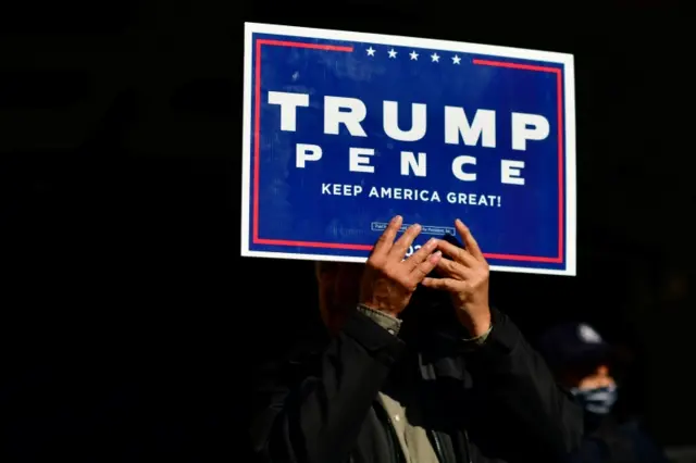 A Trump supporter clutches a campaign sign with both hands, 6 November