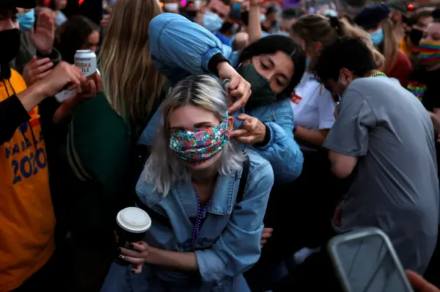 A demonstrator dances as a companion adjusts a mask in California