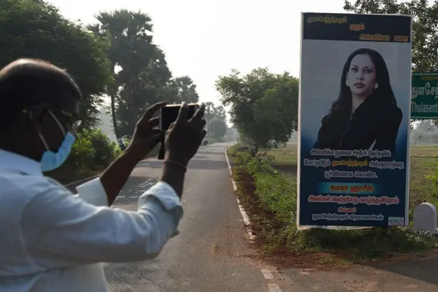 A man takes a photo of a Kamala Harris photo in her ancestral village