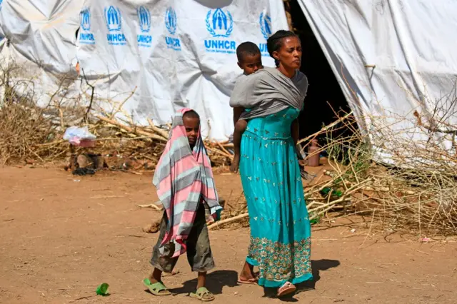 An Ethiopian refugee carries her child on her back as she walks at Um Raquba camp in Sudan's eastern Gedaref province, on November 28, 2020.