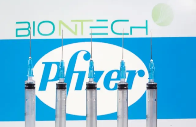 Syringes are seen in front of the Pfizer logo