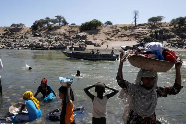 Refugees stand on the Ethiopian bank of a river that separates Sudan from Ethiopia