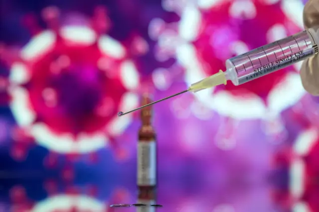 A syringe with a bubble coming out of it and coronavirus shape in background