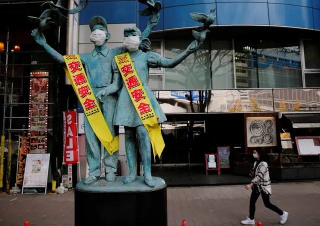 A woman wearing a mask walks past statues wearing masks in Tokyo