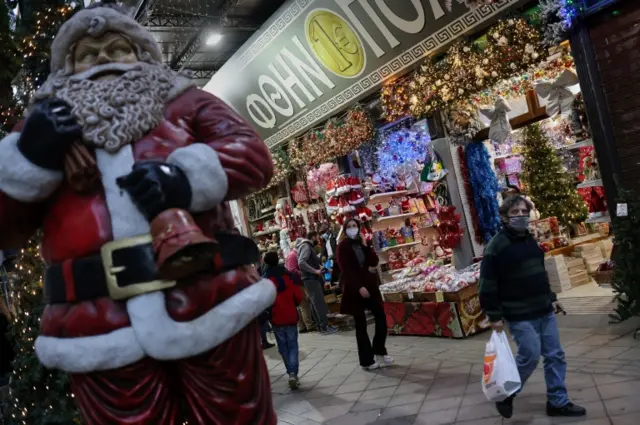 People wearing masks walk past Christmas decorations in Athens