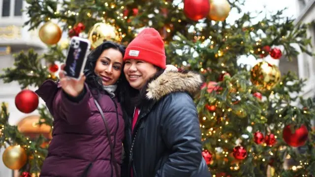 Two women take a selfie in front of a Christmas tree