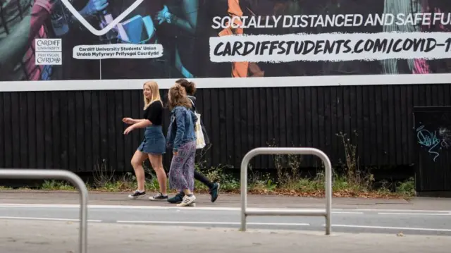 Three students walk past billboard in Cardiff