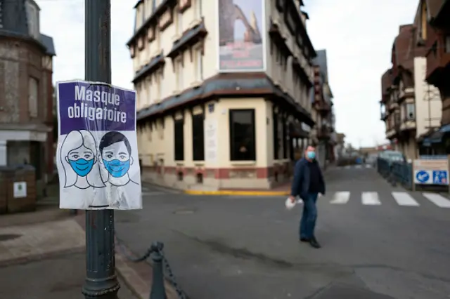 A man wearing a face mask walks by a COVID-19 precaution sign on November 07, 2020 in Etretat, France.