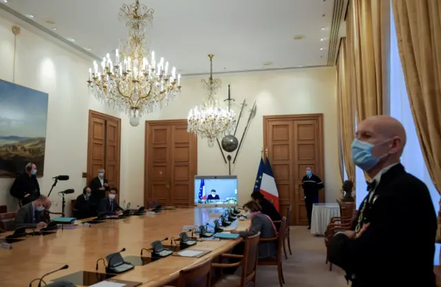 France's President Emmanuel Macron is seen on a screen as he attends by video conference a roundtable for the weekly cabinet meeting of the government at the army ministry in Paris, France, on 21 December 2020