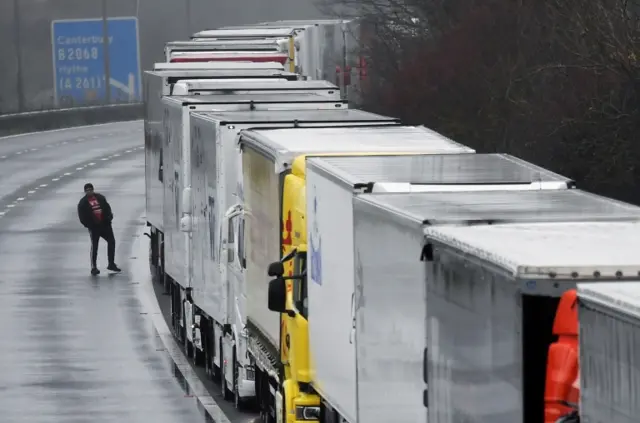 A driver walks next to lorries parked on the M20 motorway towards Eurotunnel and the Port of Dover amid travel restrictions