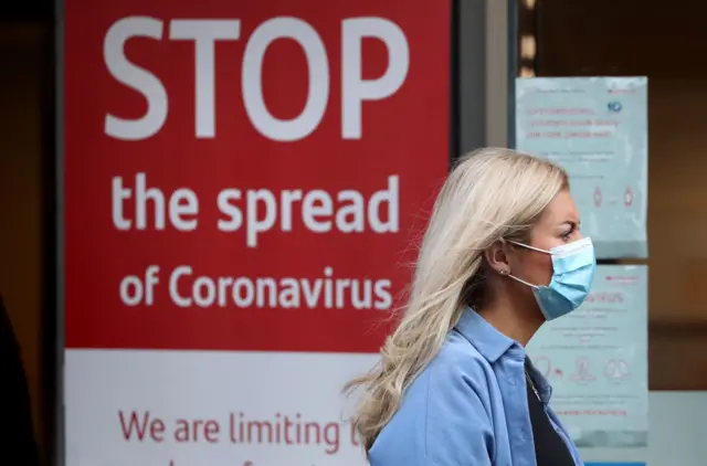 Woman walking past a sign about stopping the spread of Covid-19