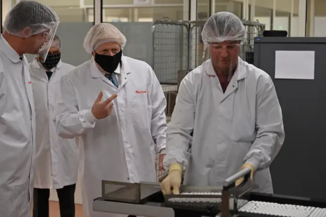 Prime Minister Boris Johnson watches a worker perform quality testing at the "fill and finish" stage of the manufacturing process of Covid-19 vaccines, during a visit to Wockhardt's pharmaceutical manufacturing facility in Wrexham, North Wales