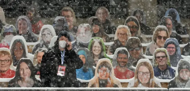 An employee stands in front of cardboard figures placed in empty stands at a ski jumping tournament in Germany