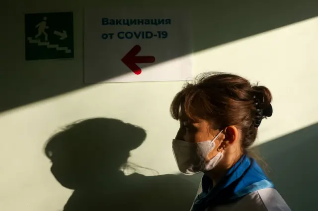 A medical worker walks past a sign giving directions to the room where COVID-19 vaccination takes place