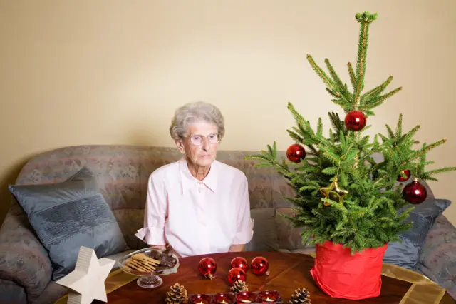Elderly woman on her own with Christmas decorations and tree