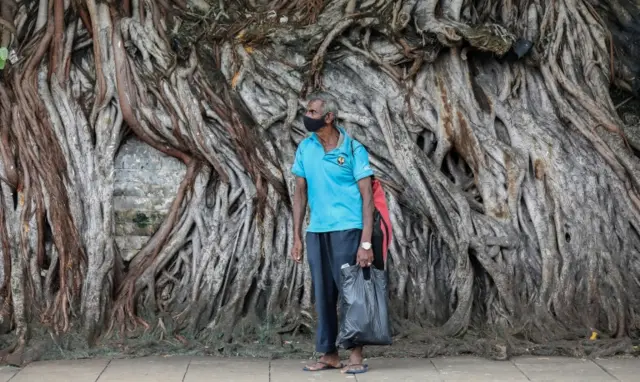 A man wearing a face mask waits for a bus at a roadside in Colombo, Sri Lanka