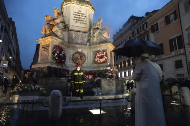 Pope Francis holds an umbrella as he prays at a statue in central Rome