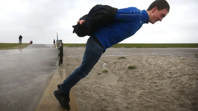 A man stands on the edge of a seawall and leans into the wind in Harlingen in the Netherlands