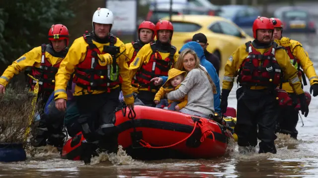 Members of the emergency services evacuate residents from flooded houses by rescue boat in south Wales.