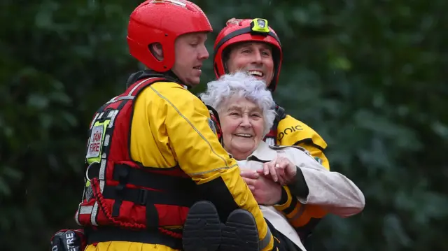 Members of the emergency services evacuate an elderly resident from a flooded house