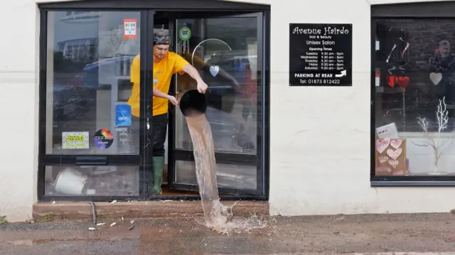 A man empties a bucket of water from a shop in Wales