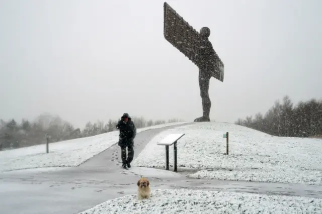 A man walks his dog past the snow-covered Angel of the North