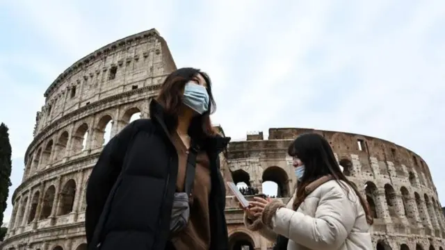 Travellers wearing surgical masks in front of the Coliseum