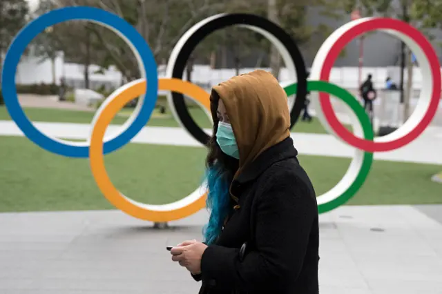 A woman wearing a face mask walks past the Olympic rings