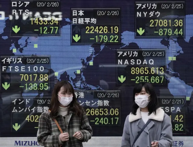 Pedestrians walk past a display showing information of global stock markets