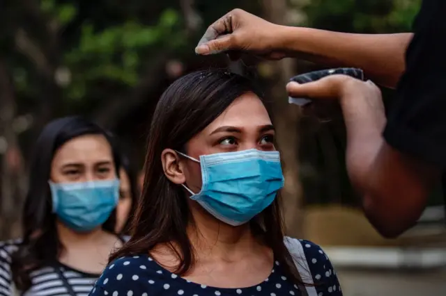 Catholic devotees wearing protective masks fall in line to have their head sprinkled with ash