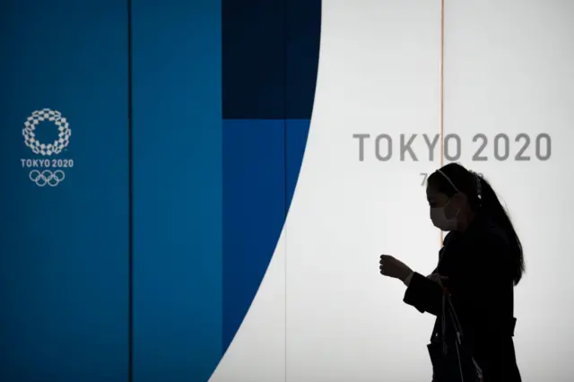 A pedestrian wearing a face mask walks past a display promoting the upcoming Tokyo 2020 Olympic and Paralympic Games