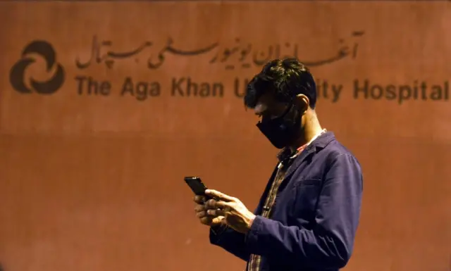 A Pakistani journalist wearing a protective facemask uses his mobile phone outside the Aga Khan University Hospital where a patient of the COVID-19 novel coronavirus has been admitted in Karachi on February 26, 2020.