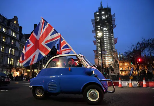 A man waves union flags from a small car as he drives past Brexit supporters in London