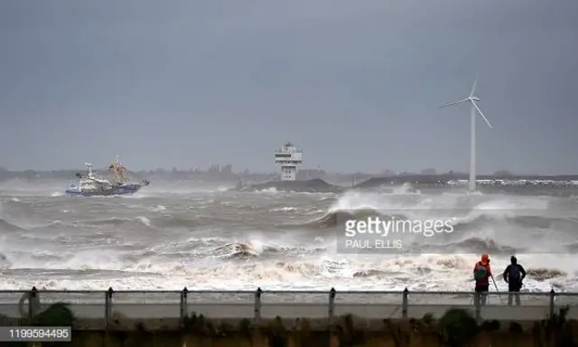 People watch as a fishing boat navigates stormy seas