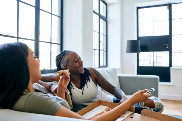 Two women watch TV with a pizza