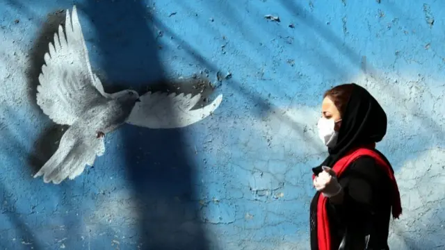 Iranian woman walks past mural in Tehran