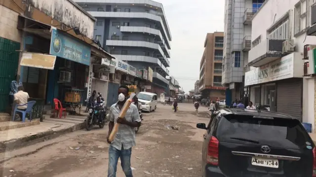 A man walks down a street in Kinshasa wearing a face mask and holding a baguette.