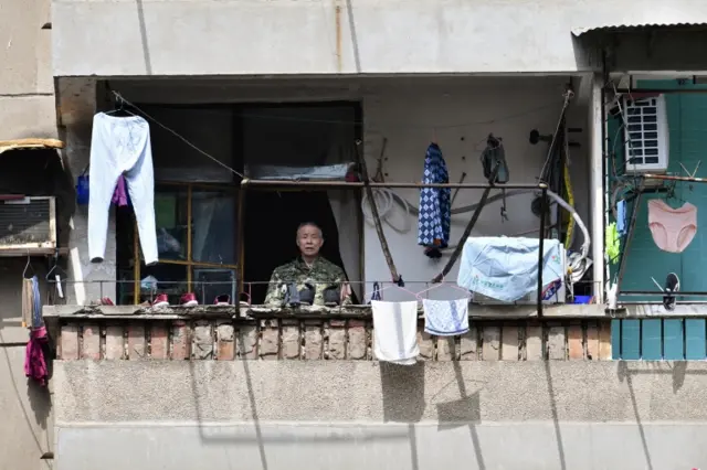 An elderly man stands on a balcony at a residential compound in Wuhan