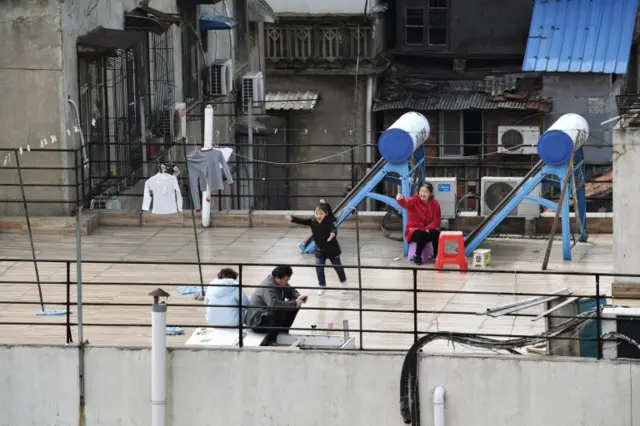 A child plays next to adults sitting on the roof terrace of a building at a residential compound in Wuhan