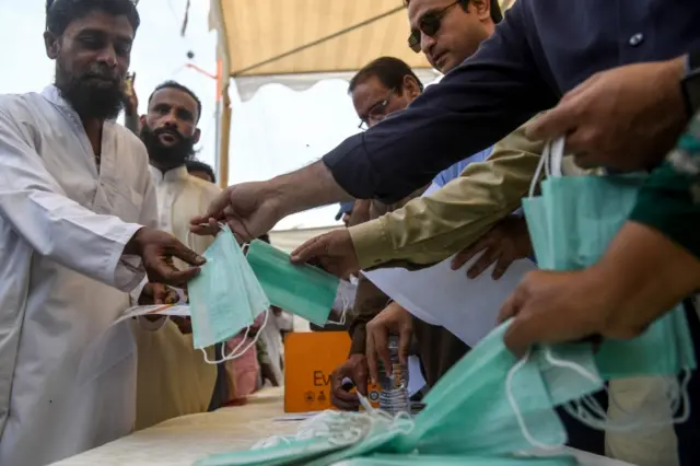 Workers of ruling Pakistan Tehreek-e-Insaf (PTI) political party, distribute facemasks and pamphlets about basic protective measures against the COVID-19 coronavirus to residents along a street in Karachi on March 10, 2020.