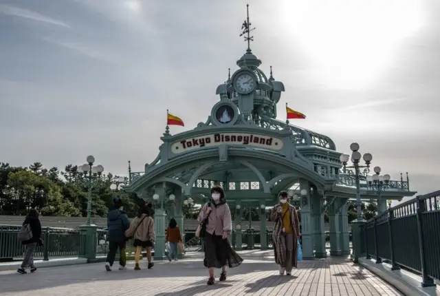 People pass beneath an archway leading to Tokyo Disneyland