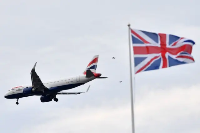 A Union flag flutters in the breeze as a British Airways passenger plane comes into land at Heathrow