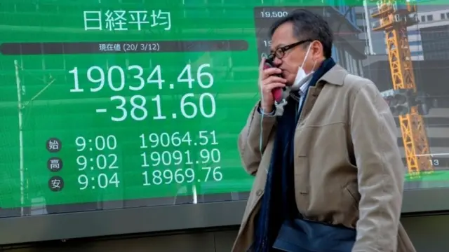 Man walking past stock market board in Tokyo (12 Mar 2020).