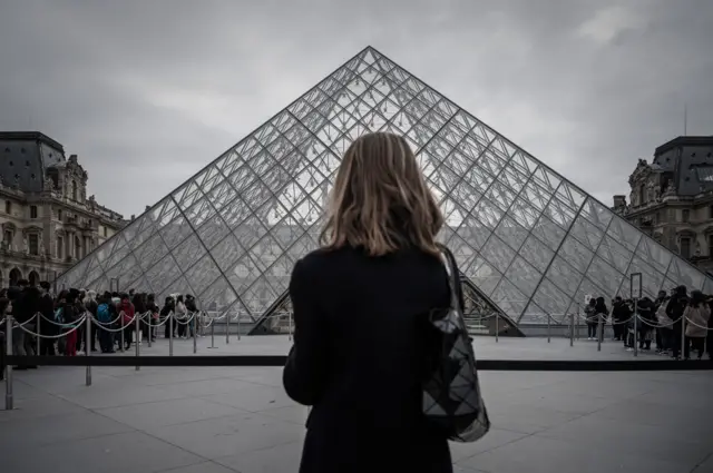 A woman stands in front of the Pyramid, the main entrance to the Louvre museum in Paris, 4 March 2020