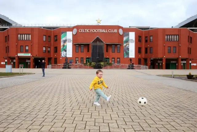 Toddler plays with football outside Celtic Park football ground in Glasgow, Scotland