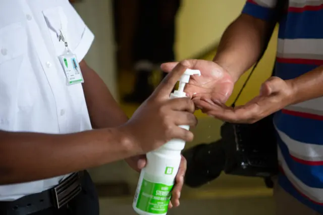 A security guard at entrance 5 with mask sanitises people's hands during the media briefing to discuss the first case of Covid-19 at Tygerberg Hospital in the Western Cape