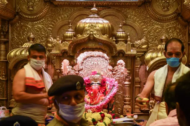 Hindu priests, wearing facemasks amid concerns over the spread of the COVID-19 novel coronavirus, stand next to an idol of Lord Ganesha as devotees lineup to pray at the Siddhivinayak temple in Mumbai on March 13, 2020.