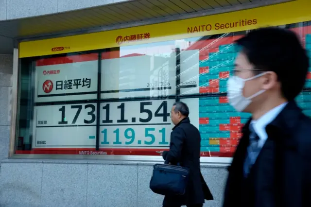 Pedestrians pass a stock markets board in Tokyo (16 March 2020).