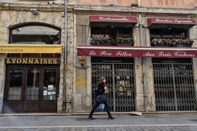 A woman walks past a closed restaurant, in the streets of Lyon, on March 16, 2020 during a COVID-19 outbreak hitting Europe.