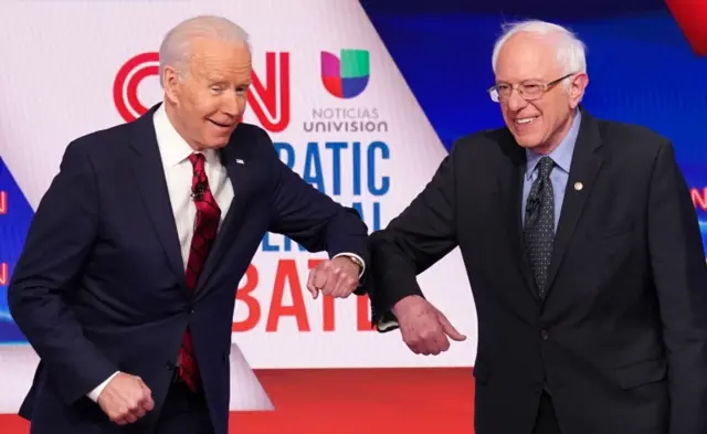 Democratic presidential hopefuls Joe Biden and Bernie Sanders do an elbow bump in place of a handshake as they greet other before the start of a debate.